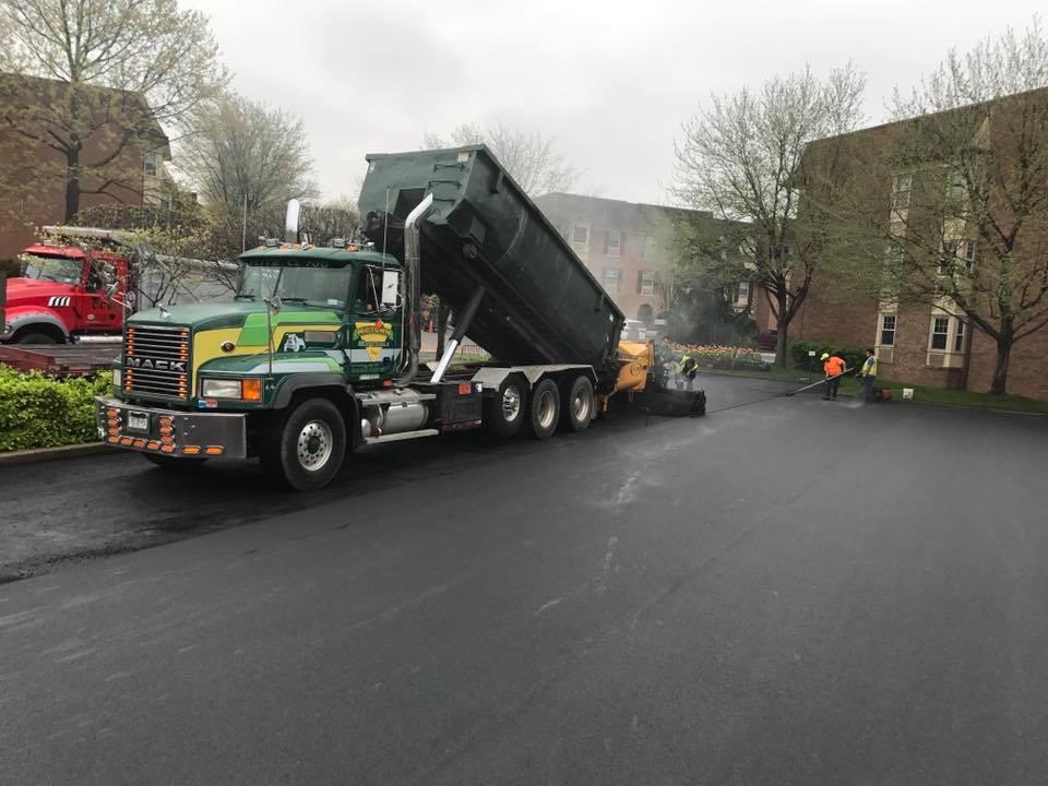 Industrial asphalt paving with dump truck feeding a paver at a warehouse yard